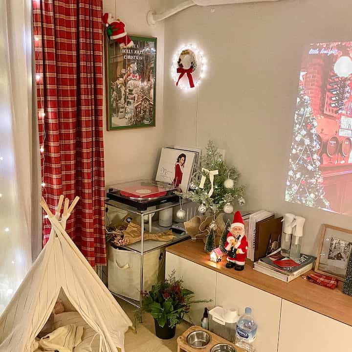 白と赤のトーンのリビング、クリスマス飾りとモジュラーシェルフ、プロジェクターが配置された雰囲気のある年末のインテリア