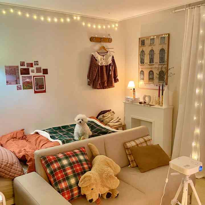 Cozy living and bedroom space with warm white walls, cushions, blankets, and soft lighting creating a festive ambiance