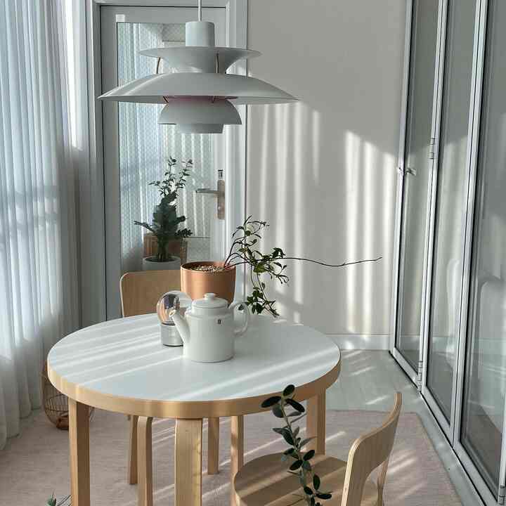 White and natural wood tone veranda home cafe featuring a round table with white teapot, creating a cozy atmosphere