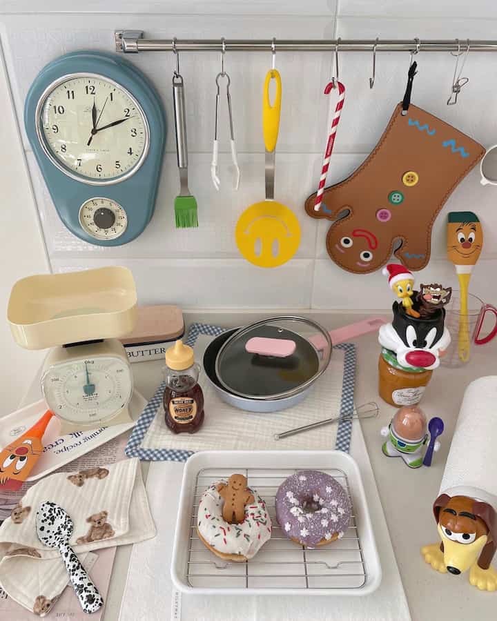 白とパステル調のキッチン、壁時計や調理器具、フライパン、クリスマス装飾が配置された雰囲気のあるインテリア