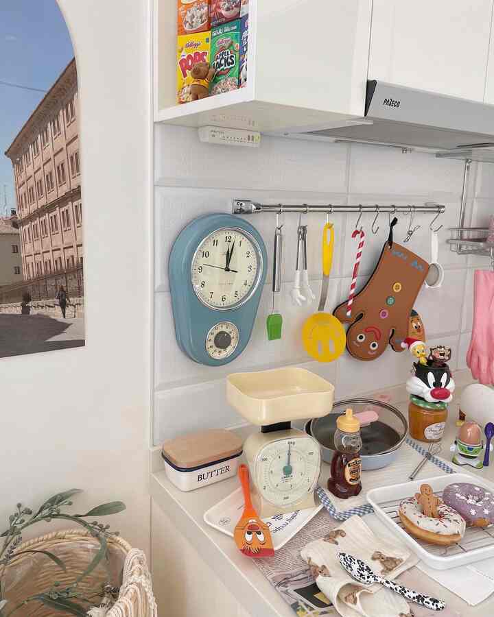 White kitchen space featuring various cooking utensils, vintage clock, and neat layout with cozy atmosphere
