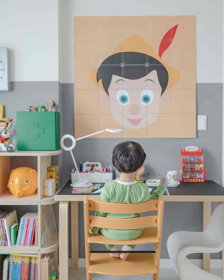 A gray and natural wood toned kids' room featuring an Artek desk, Tripp Trapp chair, and a large Pinocchio wall mural creating a cozy study area