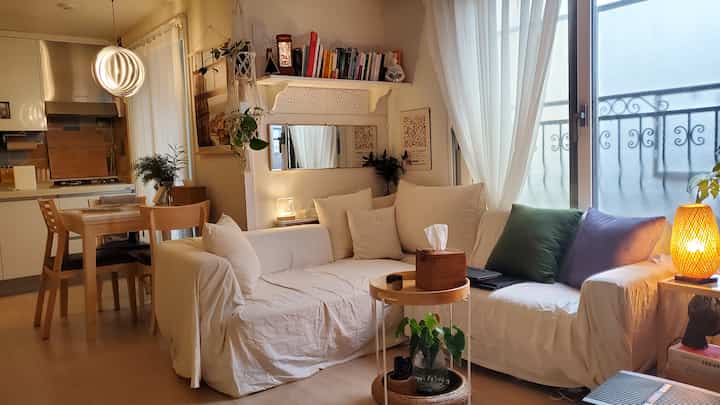 A white and wood tone living room featuring a large white sofa, rattan lamp, and dining table, creating a cozy natural atmosphere