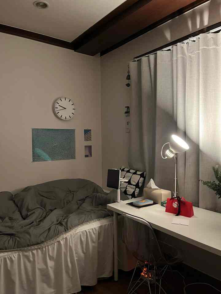 Monotone gray and white small bedroom with bed, desk, and a standing lamp creating a cozy atmosphere