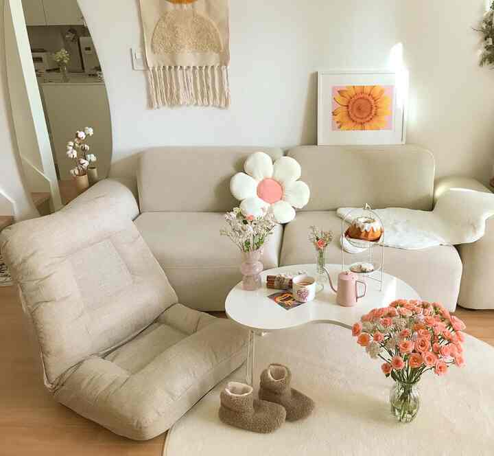 柔らかなベージュの色調の小さなリビング、ナチュラルでシンプルなソファと花飾りのテーブルが置かれた印象的な空間