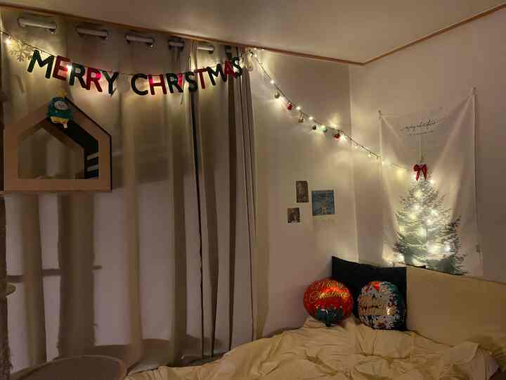 暖かいベージュ色調のワンルーム、クリスマスガーランドとライト、キャットハウス、布団が配置された雰囲気のあるインテリア