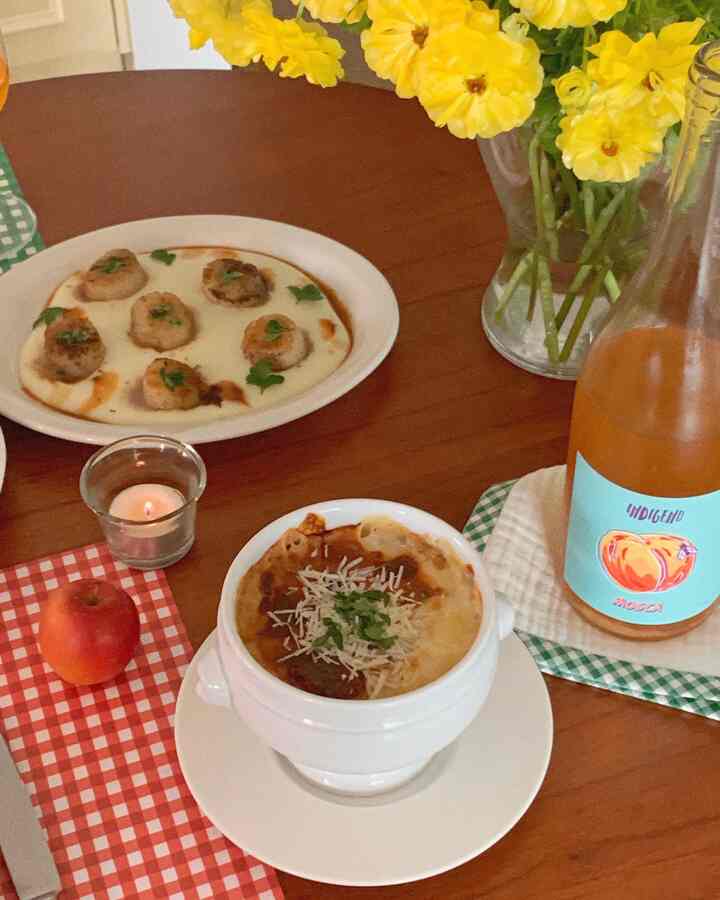 温かみのあるウッド調のテーブルに料理と黄色い花の花瓶が配置された、居心地の良いキッチンのホームパーティー空間