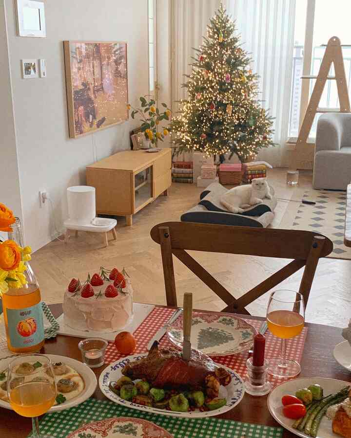 温かみのあるウッドトーンのリビング、装飾されたクリスマスツリーとホームパーティー用のダイニングテーブル、ペットベッドでくつろぐ猫が配置されたインテリア