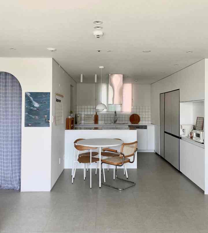 Bright white toned modern kitchen featuring a round dining table and rattan armchair arranged in a clean, minimalistic interior
