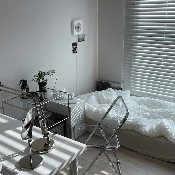 ホワイトと透明素材を基調としたコンパクトな寝室、ベッドとデスクが配置されたモダンで清潔感のあるインテリア