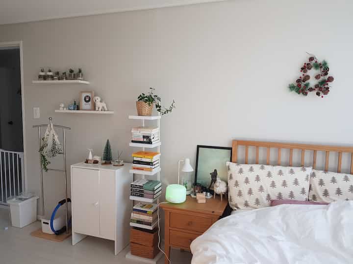 White and natural toned bedroom featuring a wooden bed, nightstand with art and mood humidifier creating cozy atmosphere