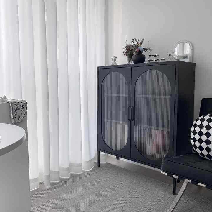 A modern studio apartment in white and black tones featuring a black cabinet with textured glass and patterned cushions, creating a clean interior