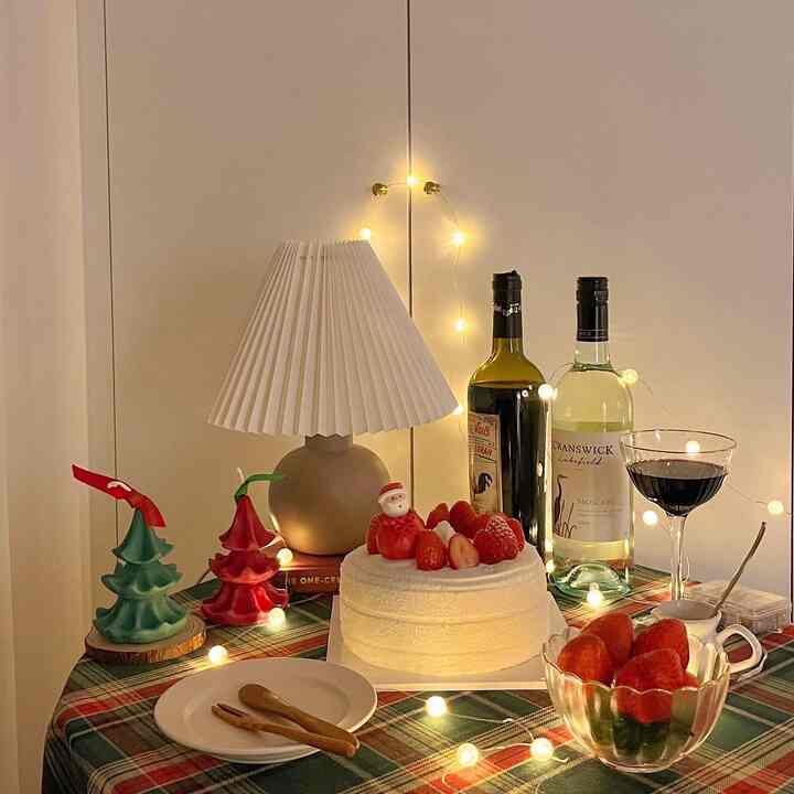 White and red themed bedroom home party table featuring cake, wine bottles, and string lights creating cozy Christmas ambiance