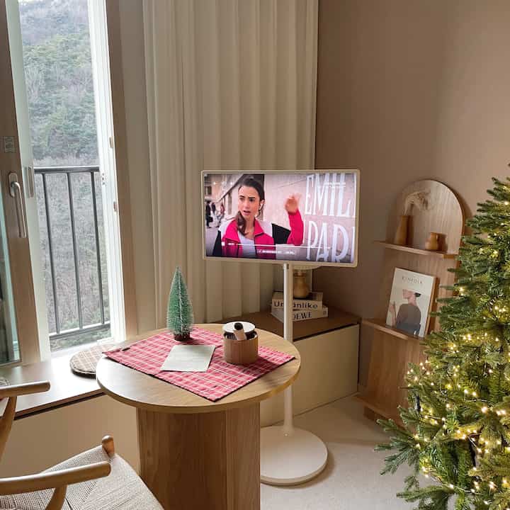 Wood tone and white living room home cafe featuring round dining table, TV, and Christmas tree with warm ambiance