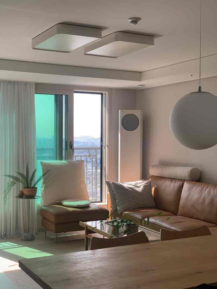 Beige and brown toned living room featuring a leather sofa, dining table, companion plant, and pendant light with a warm atmosphere