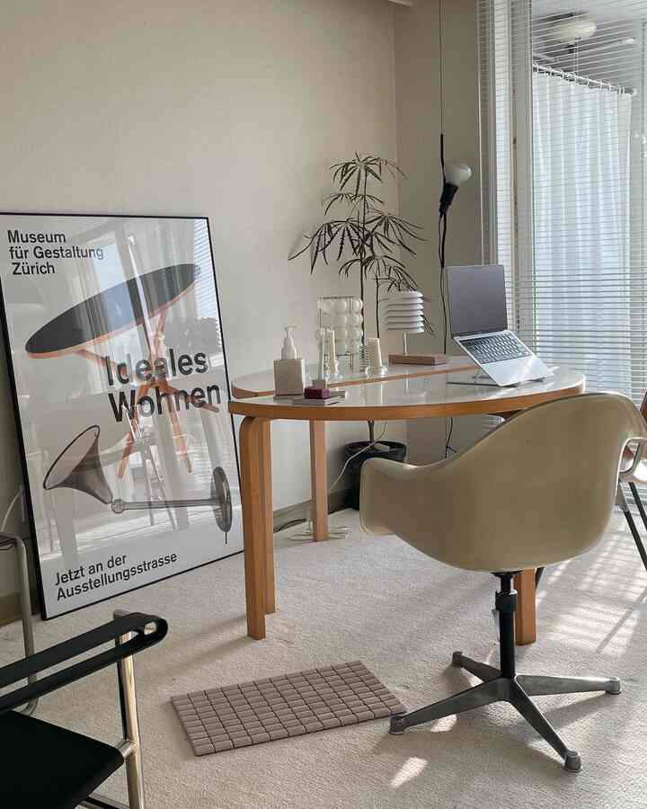 White and light brown toned home office featuring a wooden desk, office chair, plant, and blinds with a clean interior design