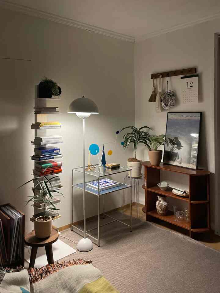 白とナチュラルカラーのリビングコーナー、本棚とフロアランプ、植物が配置されたシンプルモダンなインテリア