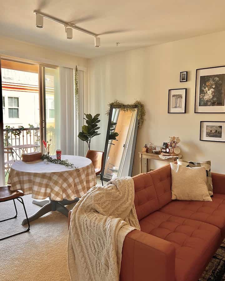 ベージュの壁とブラウンの家具が調和するリビング、丸いダイニングテーブルとソファ、額縁と全身鏡が配置されたナチュラルモダンなインテリア