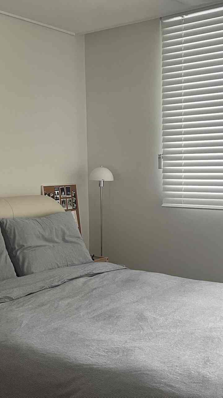White and gray toned bedroom featuring wood blinds, simple bed frame, and a floor lamp creating a cozy atmosphere