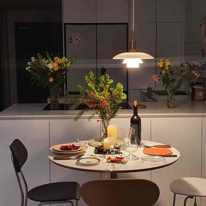 White-toned dining room featuring round table with Christmas decorations, candles, and wine bottle in a cozy atmosphere