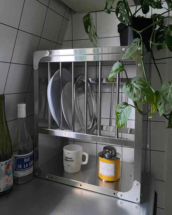 Kitchen corner with white tiled walls and stainless steel dish rack, featuring indoor plant and kitchen accessories in a calm setting