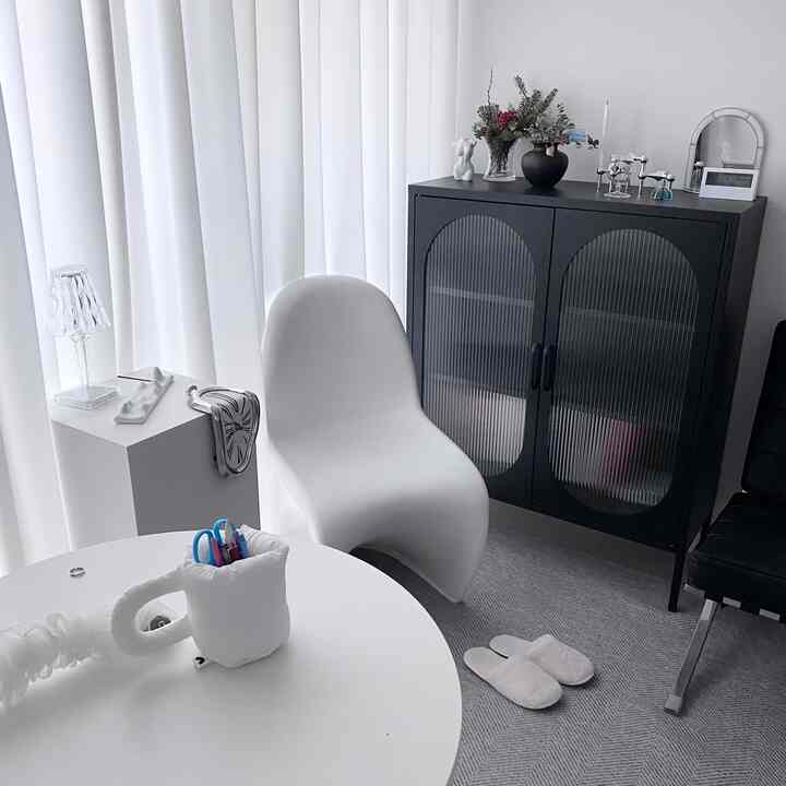 Bright white-toned living room featuring a modern white chair and black storage cabinet with elegant, minimalistic decor