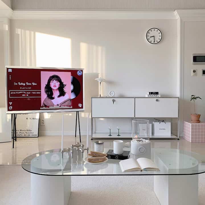 Modern living room in warm white tones, featuring a transparent glass table, sideboard, and table lamp with a cozy atmosphere