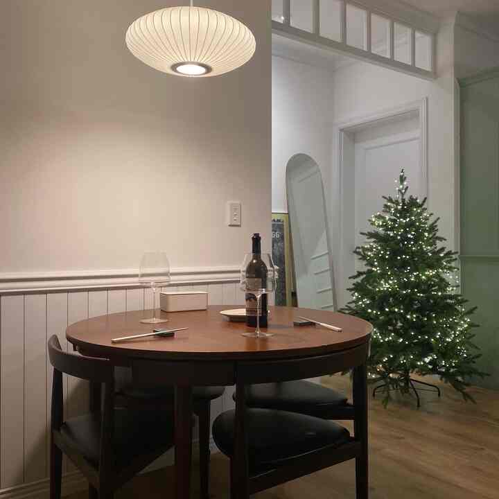 白と木目調のキッチン空間、丸テーブルと椅子、クリスマスツリーとストリングライトが暖かい雰囲気を演出するインテリア