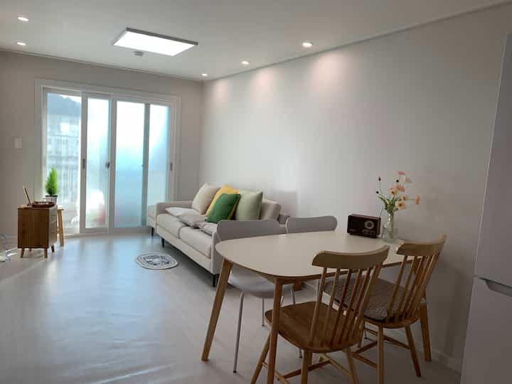 White and wood-tone two-person living and dining room featuring a sofa and oval dining table with cushions, cozy and neat atmosphere