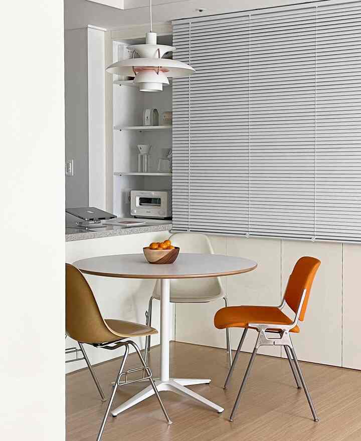 白とライトブラウンの色調のキッチンスペース、丸いダイニングテーブルと多色のチェアが配置されたモダンなインテリア