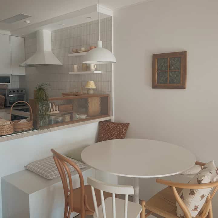 Natural color and white toned kitchen and dining area featuring a round dining table with assorted chairs and cushions creating a cozy home cafe style interior