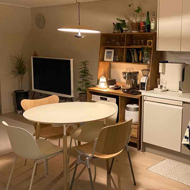 ホワイトとウッドトーンが調和したおうちカフェ、円形テーブルとナチュラルな家具、コーヒーマシンが配置された雰囲気のある空間