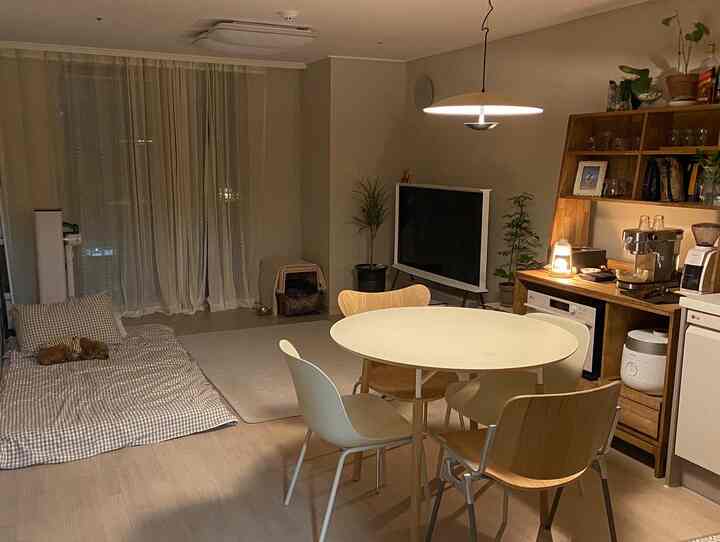 ナチュラルカラーのリビングルーム、円形のダイニングテーブル、マットレスの上でくつろぐ犬、ホームカフェ用のコーヒー器具が配置された落ち着いた空間