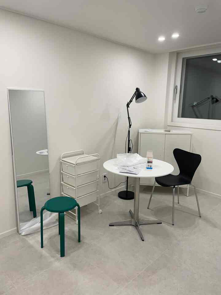 白を基調とした小さな部屋、丸テーブルと黒い椅子、スツールや収納が配置されたシンプルな空間