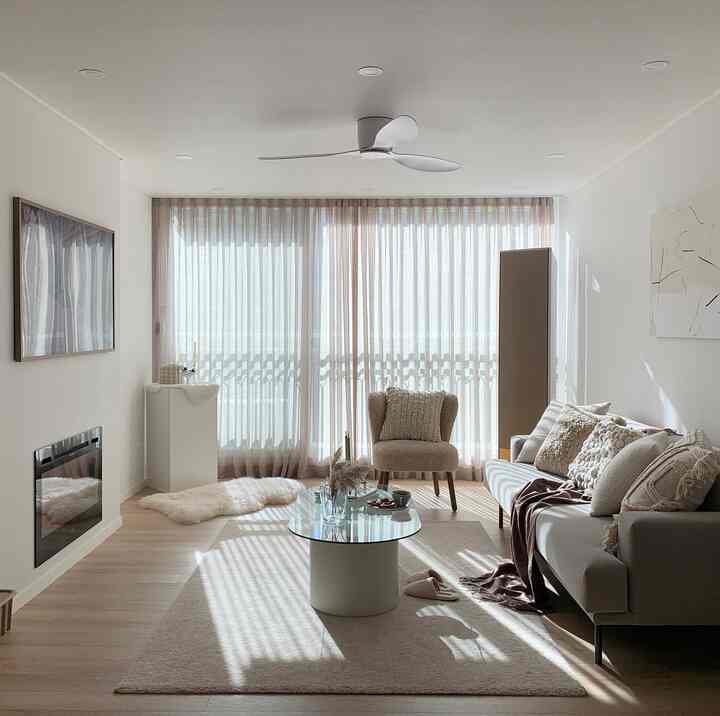 Beige-toned natural modern living room featuring an electric fireplace, glass table, and armchair creating a warm atmosphere