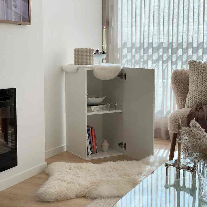 White and natural color toned living room featuring a storage cabinet, sheepskin rug, and armchair creating a cozy atmosphere