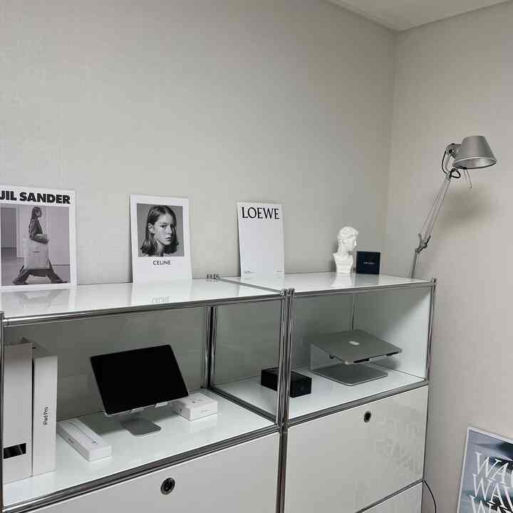 白とシルバーの落ち着いたトーンのホームオフィス、整理された収納棚とアップル製品、銀色のスタンドライトが配置された印象的な空間