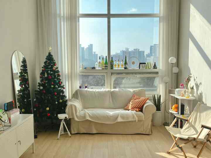 Bright white and brown toned living room with white sofa near window and decorated Christmas tree creating a cozy atmosphere