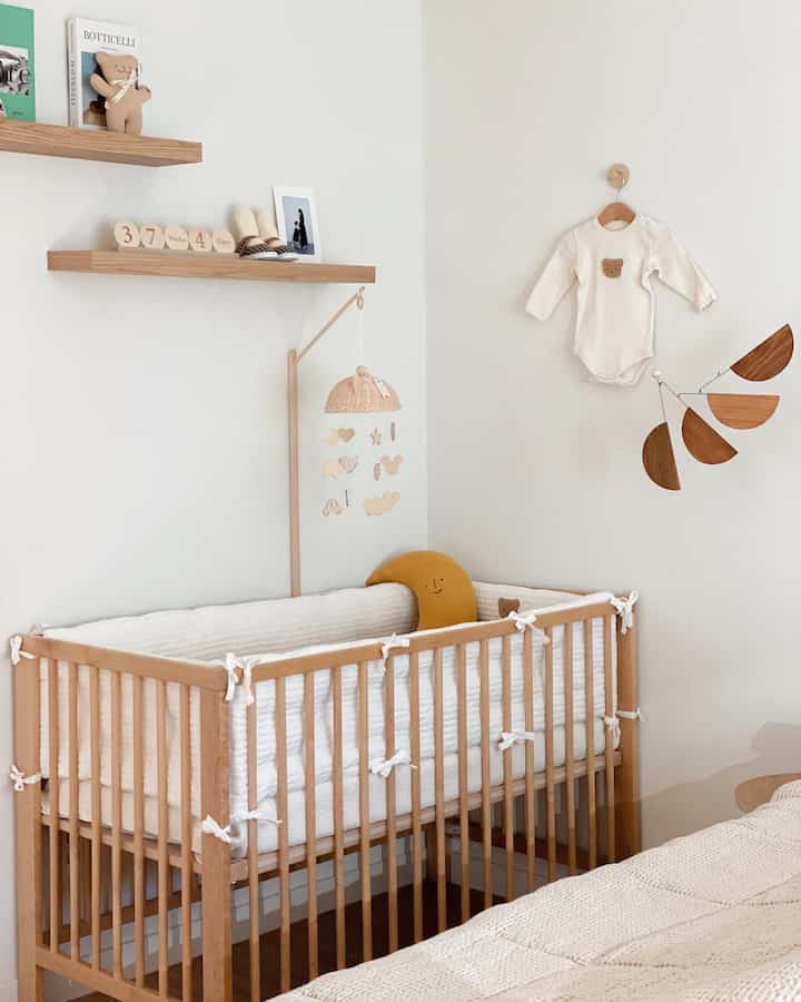 白と木目調のナチュラルな寝室、ベビーベッドとモビールが配置された赤ちゃんと暮らす空間