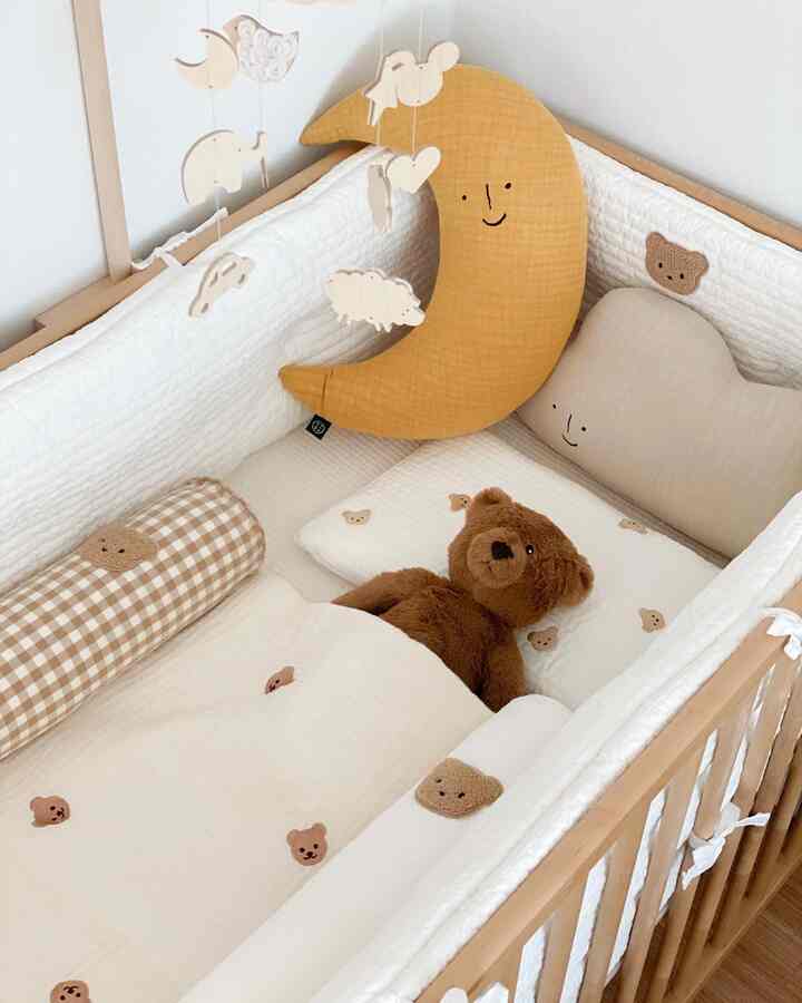 ベージュと白のトーンのベビーベッド、くまのぬいぐるみとかわいいクッションが配置された暖かい子供部屋のインテリア