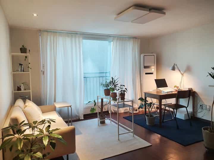 Natural tone living room and home office space in beige and white, featuring sofa, desk, and plants with a cozy atmosphere