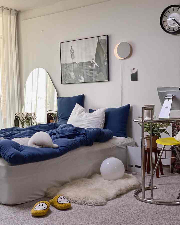 Navy and white toned bedroom with curved mirror and yellow chair, creating a cozy atmosphere