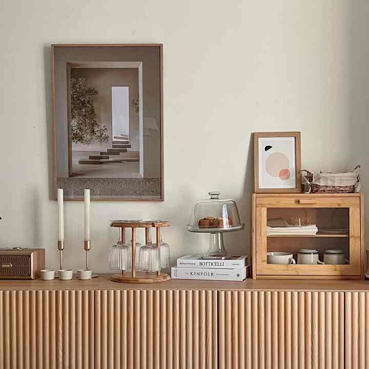 温かみのあるブラウンとアイボリーのトーンのホームカフェ兼収納キャビネットが配置された雰囲気のあるインテリア、ポスターとガラスドームのケーキスタンドでポイントを加えた空間