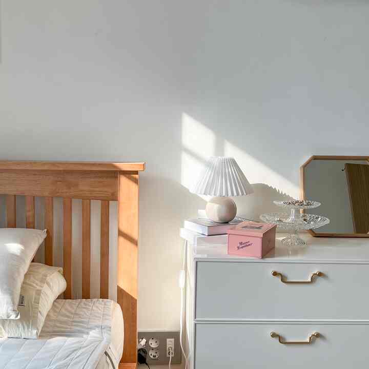白とベージュの色調の寝室、木製ベッドと白いテーブルランプ、収納家具が落ち着いた雰囲気のインテリア