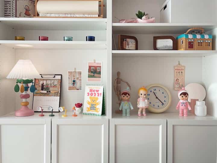 白とパステル調の子供部屋の本棚におもちゃと照明が配置された雰囲気のあるインテリア