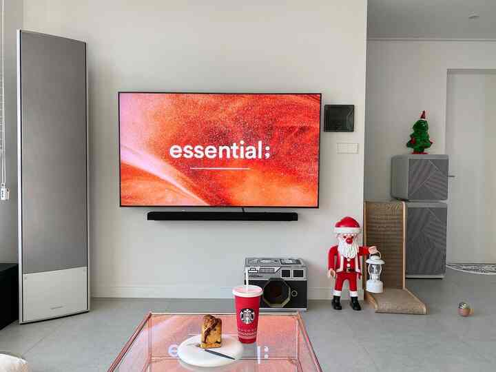 White and gray toned living room featuring wall-mounted QLED TV, cat scratching post, and home cafe setup with Starbucks drink