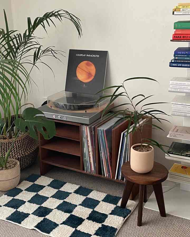ネイビーとホワイトのチェッカーボードラグが敷かれたリビングの一角に、レコード収納棚とレコードプレーヤー、多数の植物が配された自然でレトロなインテリア