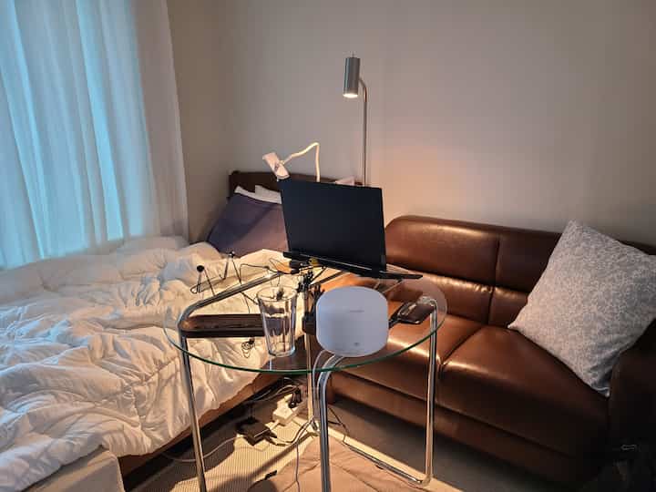 Cozy bedroom with warm natural tones featuring brown leather sofa, transparent round glass table and white bedding
