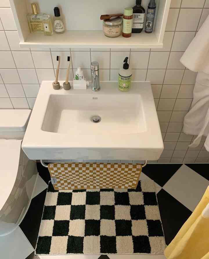 白と黒のチェッカーボードタイルが調和したバスルームの洗面台、黄色のチェックタオルと化粧品が整然と配置された雰囲気のあるインテリア
