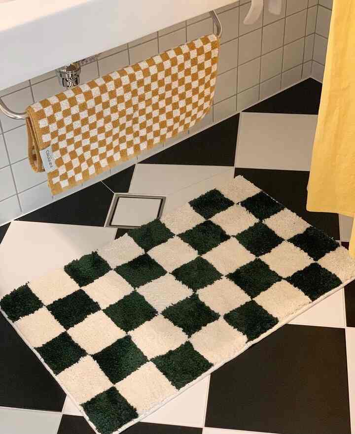 Bathroom with checkerboard pattern featuring black and white tiled floor, soft textured rug and towel creating a neat atmosphere